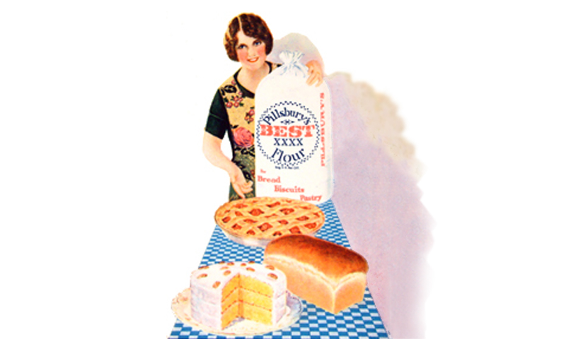 Woman at long table holding upright a bag of flour, with baked goods : bread, pie, cake.